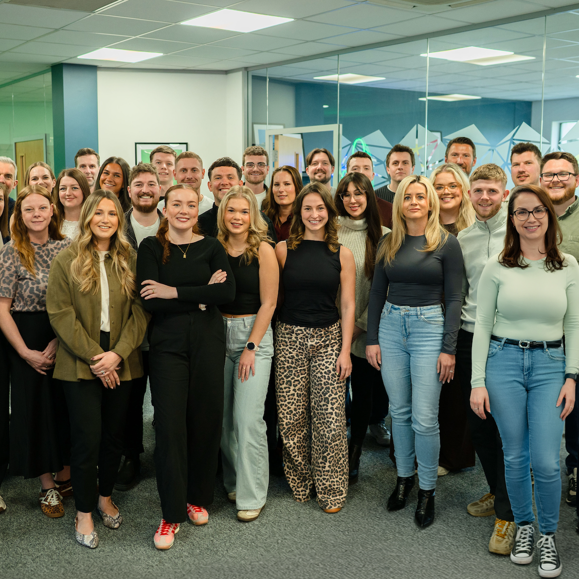 A large group of smiling colleagues standing together in a modern indoor office space